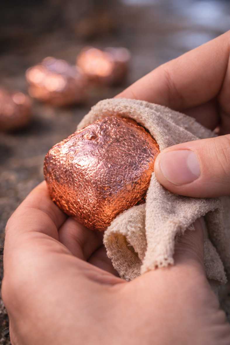 A hand polishing a copper plated Wombat Nugget with a soft cloth